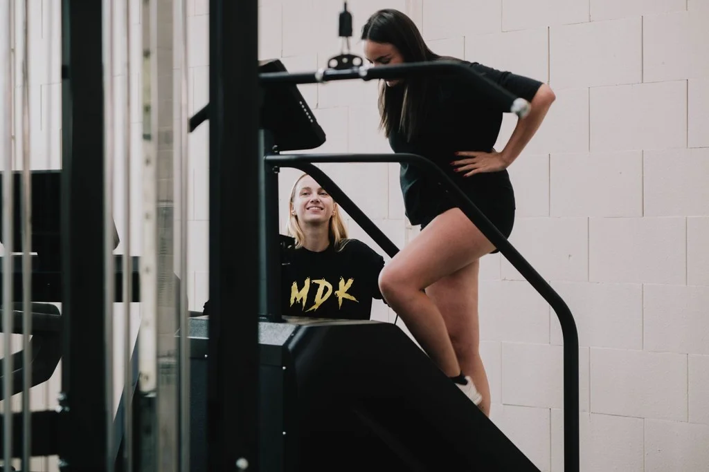 Coach in MDK-trui begeleidt een klant op de traploopmachine