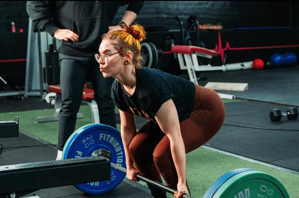 Klant doet een deadlift met de halterstang, haar coach kijkt mee