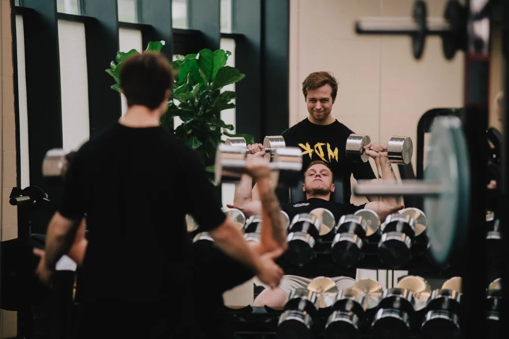 Coach kijkt toe terwijl een klant met dumbbells traint